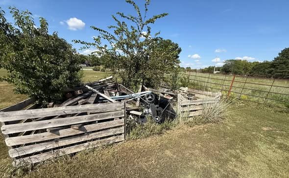 Large pile of brush, wood, and debris against a fence line before cleanup